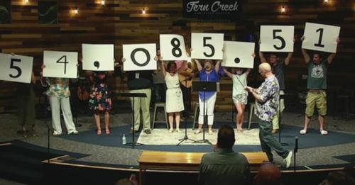 Screen shot of Fern Creek Church congregation holding up signs with numbers on the stage at church. The numbers read together as 54,085.51, indicating the dollar amount raised by the church for Safe Haven Baby Boxes in Kentucky